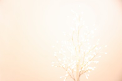 Decorative tree with lights on beige background, blurred view. Space for text