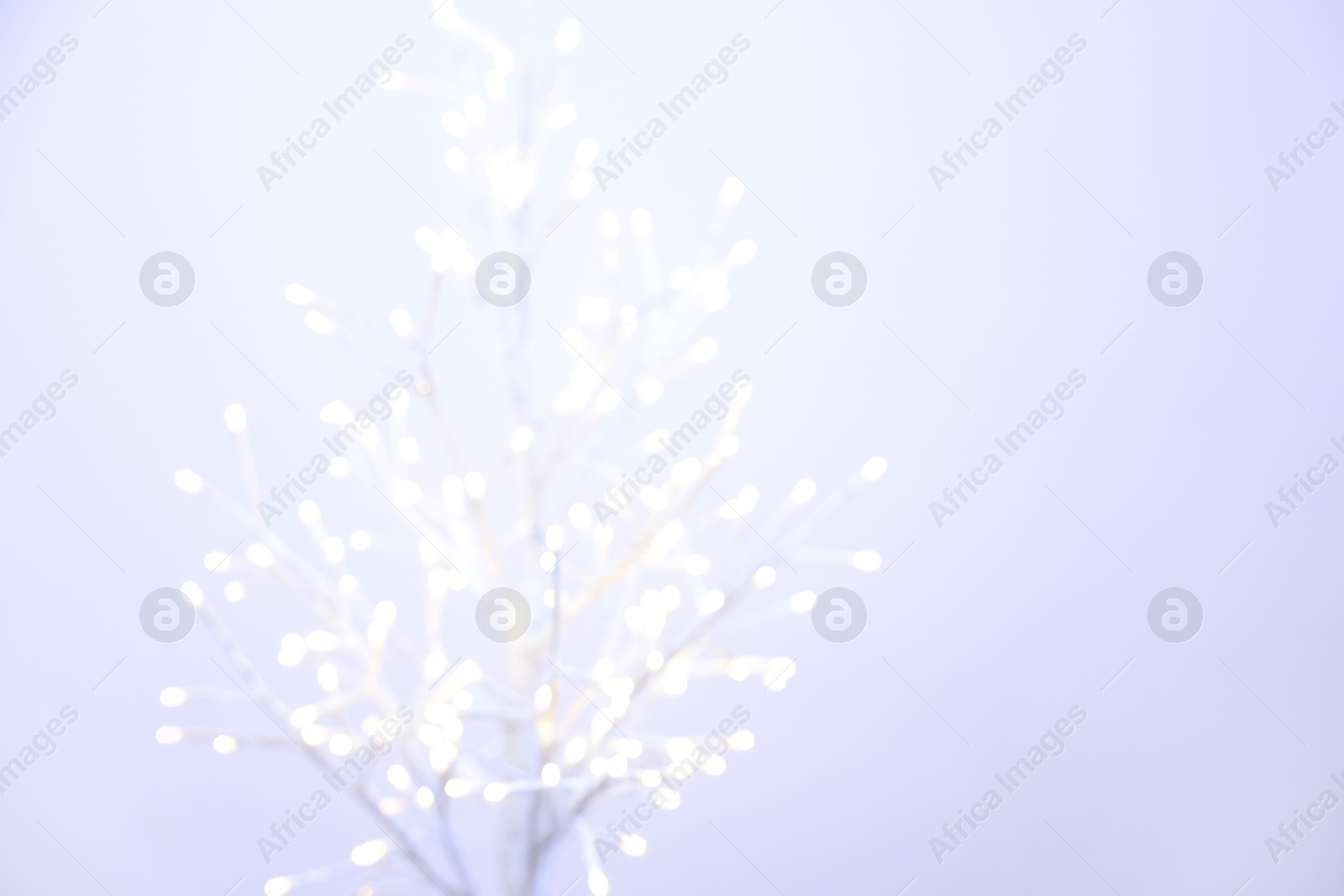 Photo of Decorative tree with lights on light background, blurred view. Space for text