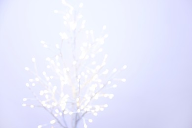 Photo of Decorative tree with lights on light background, blurred view. Space for text