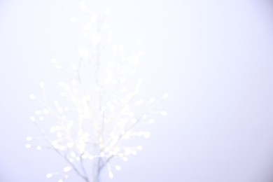 Photo of Decorative tree with lights on light background, blurred view. Space for text