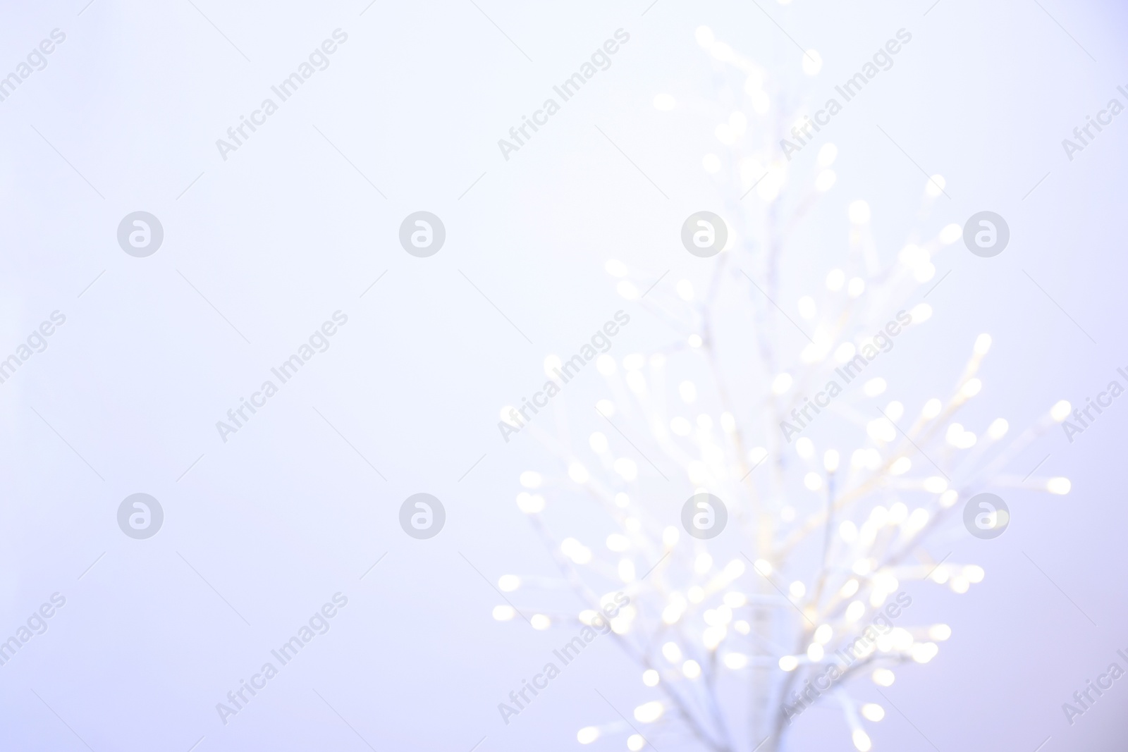 Photo of Decorative tree with lights on light background, blurred view. Space for text