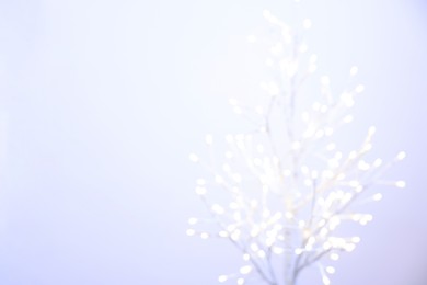 Decorative tree with lights on light background, blurred view. Space for text