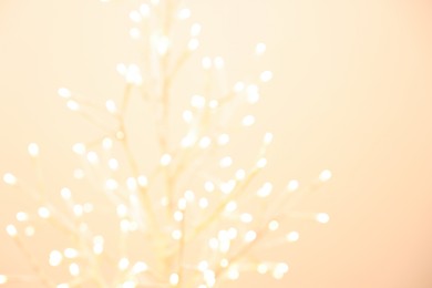 Photo of Decorative tree with lights on beige background, blurred view