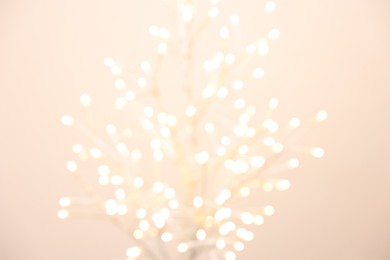 Decorative tree with lights on beige background, blurred view