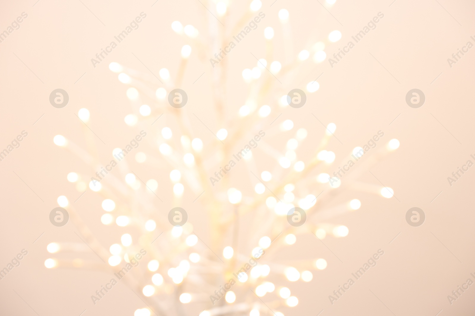 Photo of Decorative tree with lights on beige background, blurred view