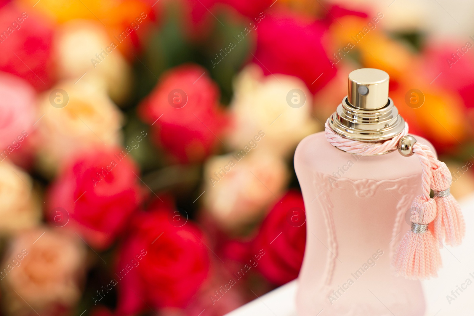 Photo of Bottle of perfume on white table against bouquet of beautiful roses, closeup. Space for text