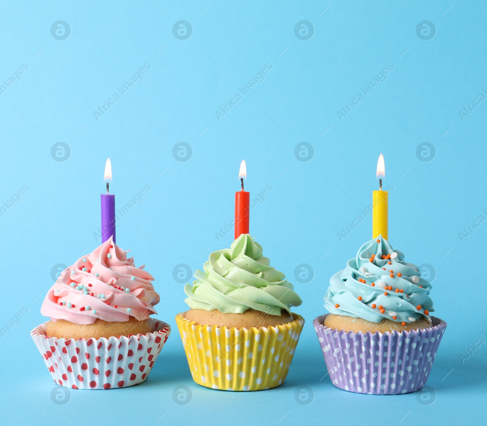 Photo of Birthday cupcakes with burning candles on light blue background