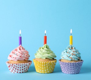 Birthday cupcakes with burning candles on light blue background