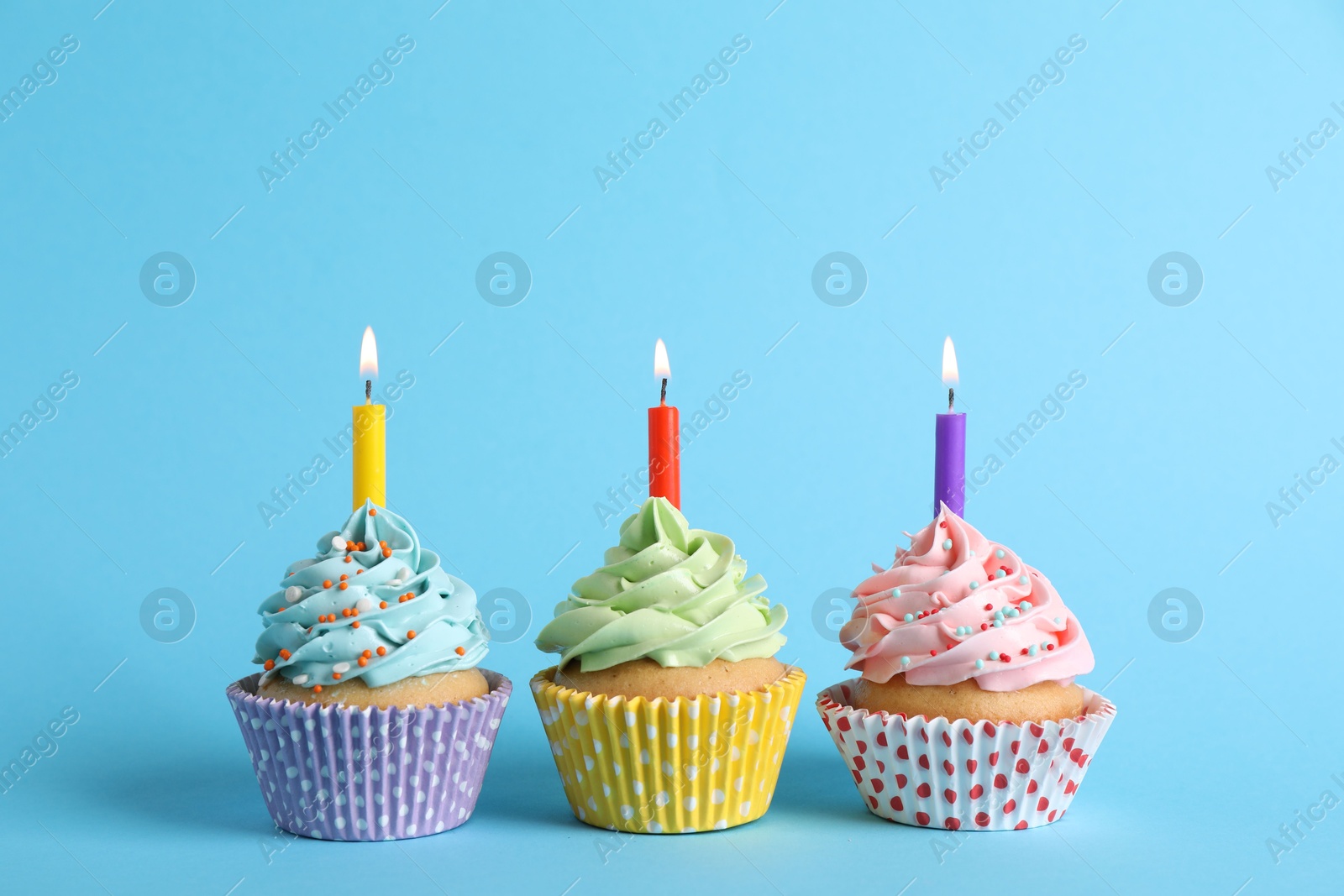 Photo of Birthday cupcakes with burning candles on light blue background