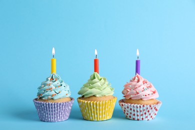 Birthday cupcakes with burning candles on light blue background