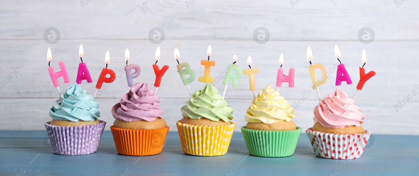 Photo of Birthday cupcakes with burning candles on blue wooden table