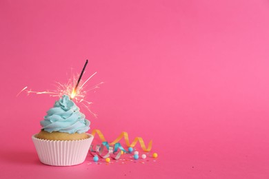 Photo of Birthday cupcake with burning sparkler and streamers on pink background. Space for text