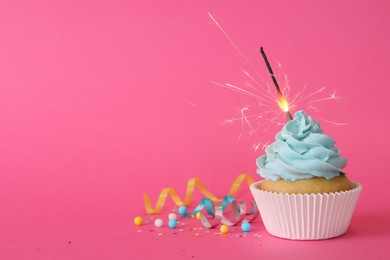 Photo of Birthday cupcake with burning sparkler and streamers on pink background. Space for text