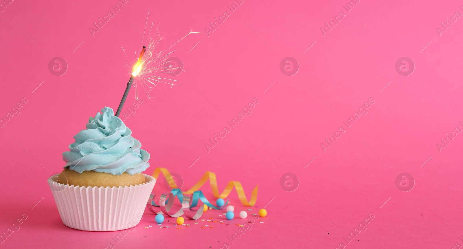 Photo of Birthday cupcake with burning sparkler and streamers on pink background. Space for text