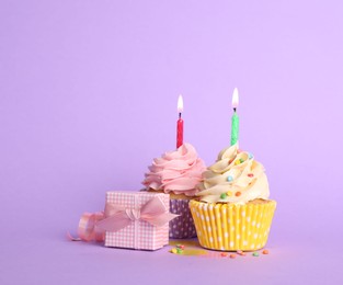 Photo of Birthday cupcakes with burning candles and gift box on violet background