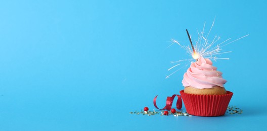 Photo of Birthday cupcake with burning sparkler on light blue background. Space for text