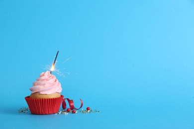 Photo of Birthday cupcake with burning sparkler on light blue background. Space for text