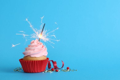 Photo of Birthday cupcake with burning sparkler on light blue background. Space for text