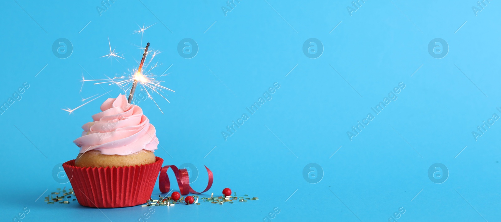 Photo of Birthday cupcake with burning sparkler on light blue background. Space for text