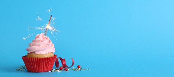 Photo of Birthday cupcake with burning sparkler on light blue background. Space for text