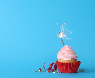 Photo of Birthday cupcake with burning sparkler on light blue background. Space for text