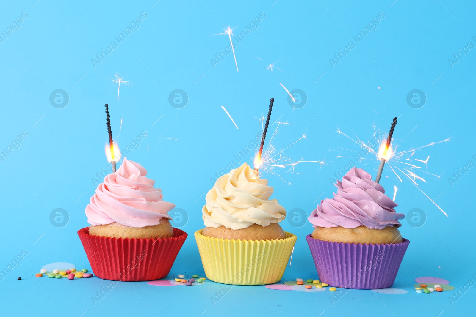 Photo of Birthday cupcakes with burning sparklers and sprinkles on light blue background