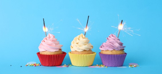 Photo of Birthday cupcakes with burning sparklers and sprinkles on light blue background