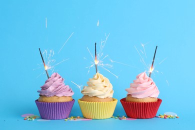 Photo of Birthday cupcakes with burning sparklers and sprinkles on light blue background