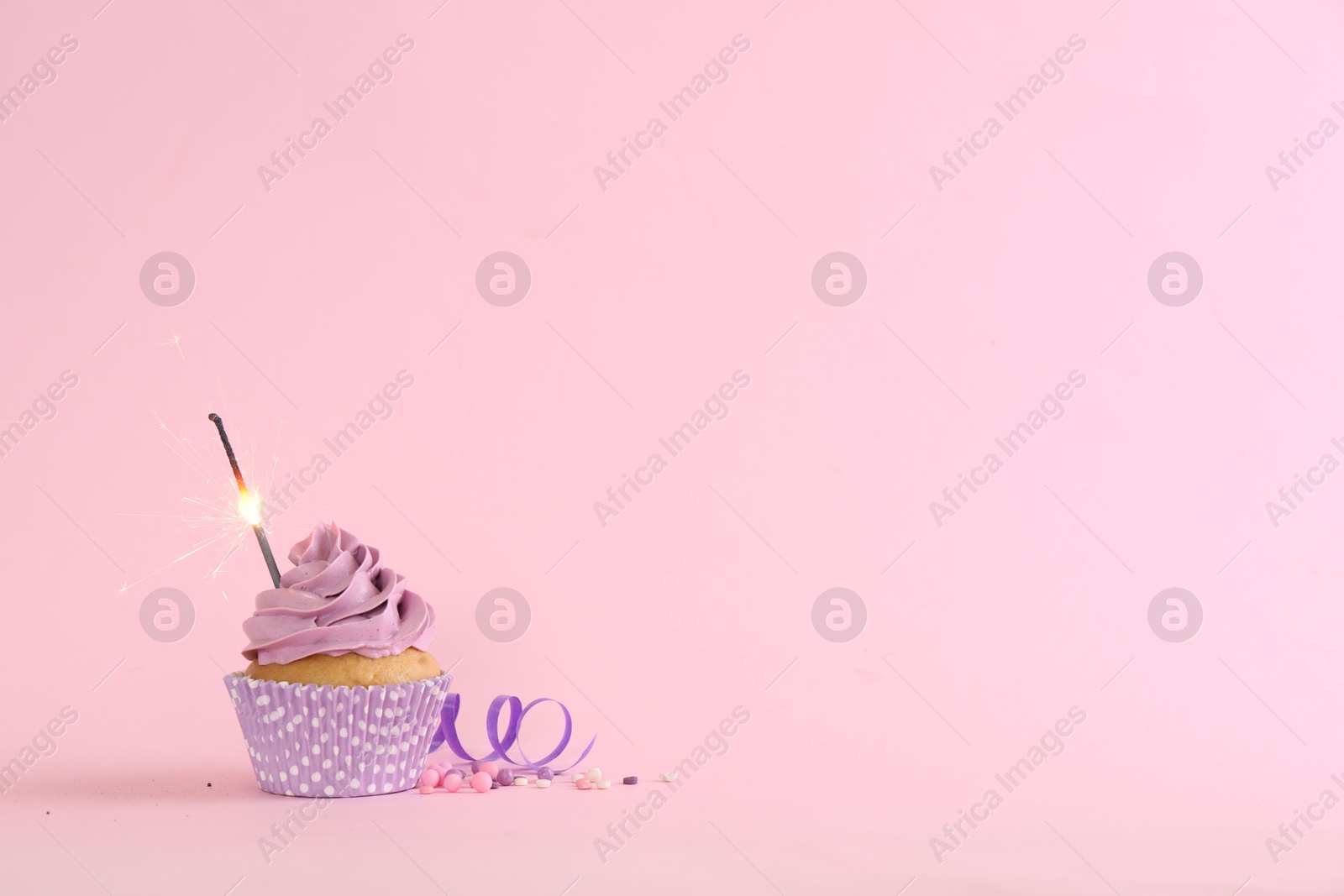 Photo of Birthday cupcake with burning sparkler, streamer and sprinkles on pink background. Space for text