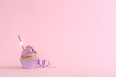 Photo of Birthday cupcake with burning sparkler, streamer and sprinkles on pink background. Space for text