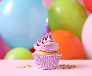 Photo of Birthday cupcake with burning candle and sprinkles on pink table against color balloons