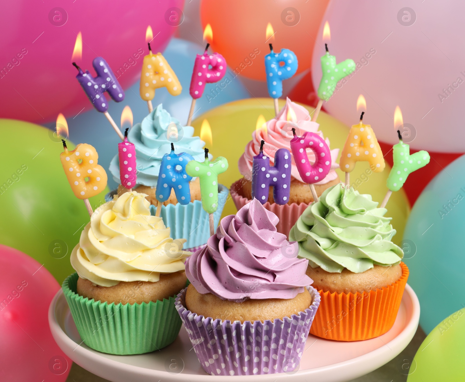 Photo of Birthday cupcakes with burning candles on stand near color balloons