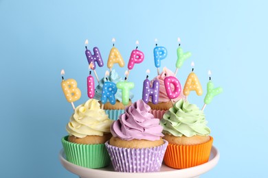 Photo of Birthday cupcakes with burning candles on stand against light blue background