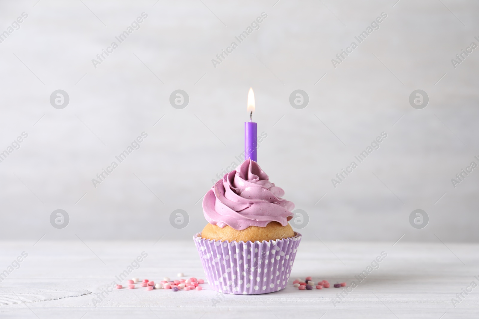 Photo of Delicious birthday cupcake with burning candle and sprinkles on white wooden table