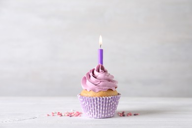 Delicious birthday cupcake with burning candle and sprinkles on white wooden table