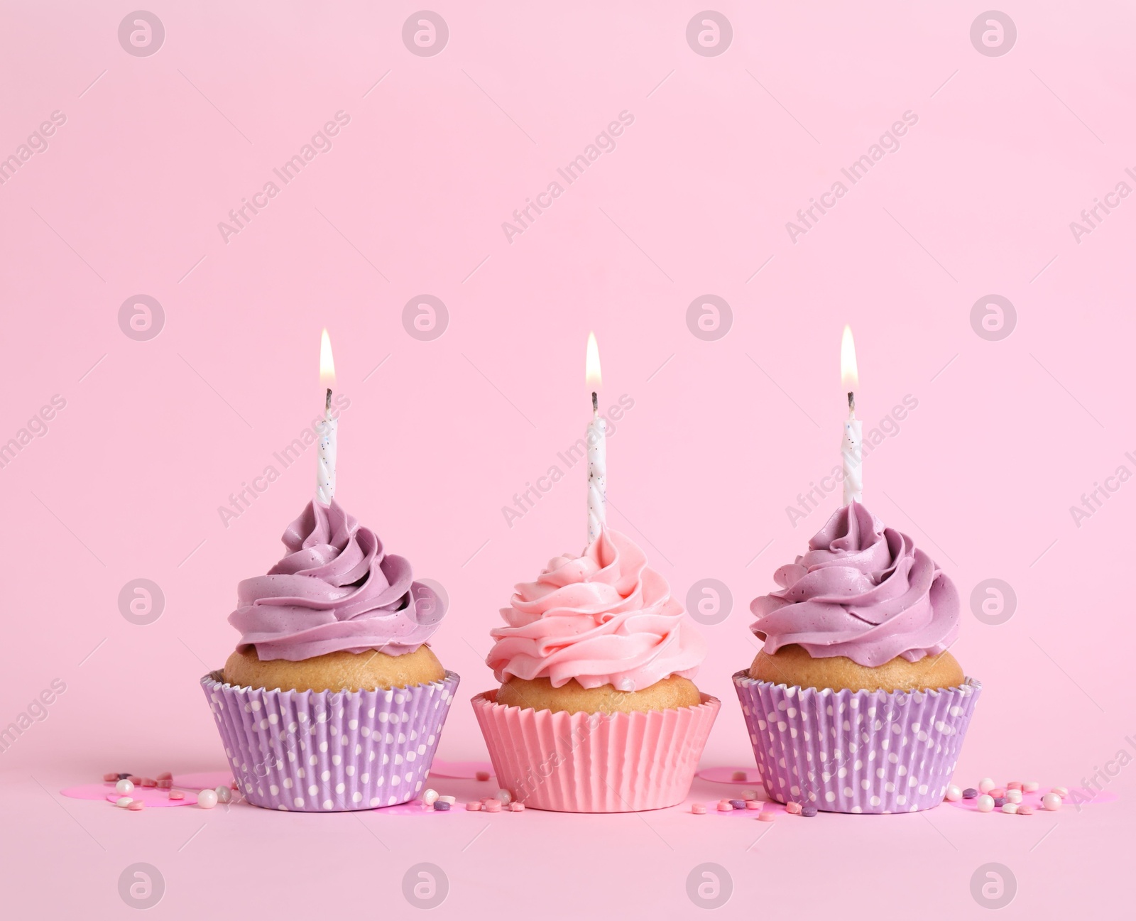 Photo of Delicious birthday cupcakes with burning candles and sprinkles on pink background