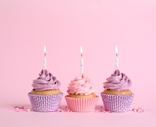 Delicious birthday cupcakes with burning candles and sprinkles on pink background