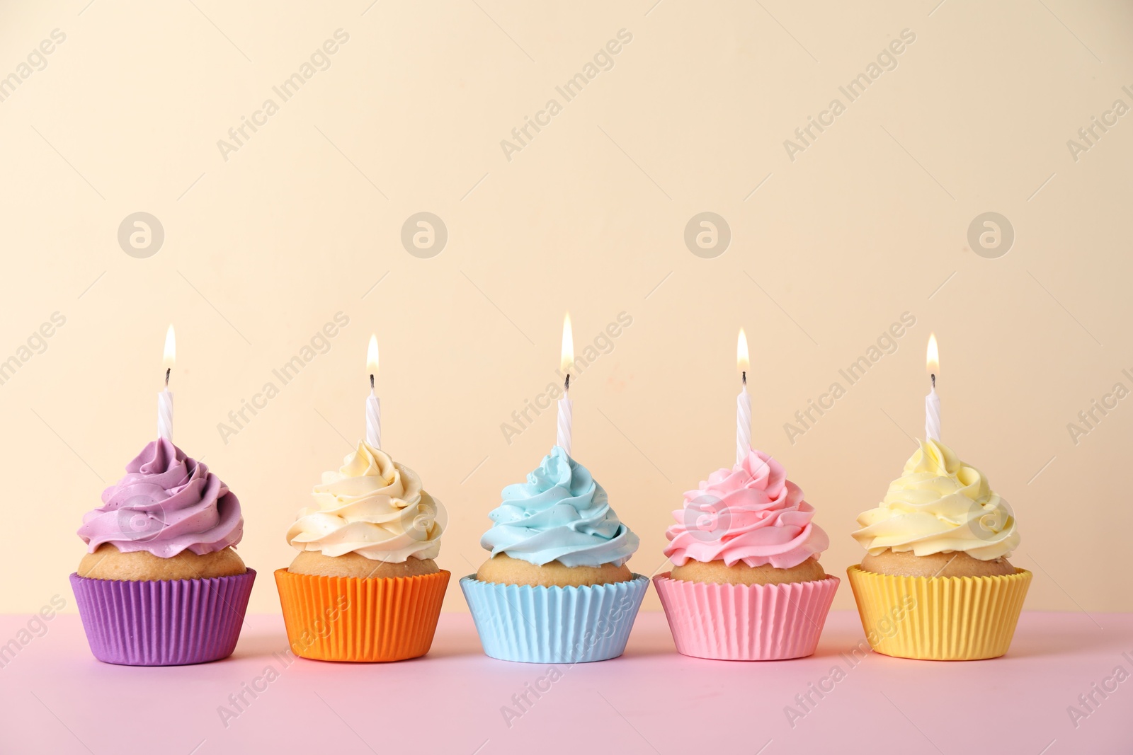 Photo of Delicious birthday cupcakes with burning candles on pink table against beige background