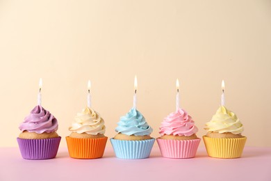 Photo of Delicious birthday cupcakes with burning candles on pink table against beige background