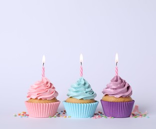 Photo of Delicious birthday cupcakes with burning candles and sprinkles on light grey background