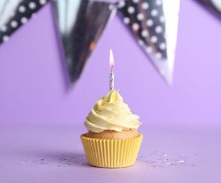 Photo of Delicious birthday cupcake with burning candle on violet background