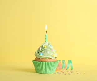 Photo of Delicious birthday cupcake with burning candle, sprinkles and streamers on yellow background