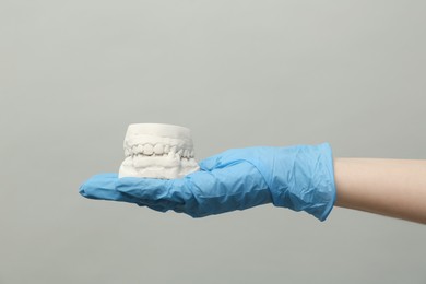 Doctor holding dental model with jaws on grey background, closeup. Cast of teeth