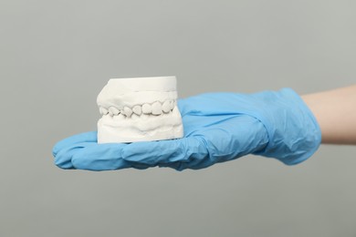 Doctor holding dental model with jaws on grey background, closeup. Cast of teeth