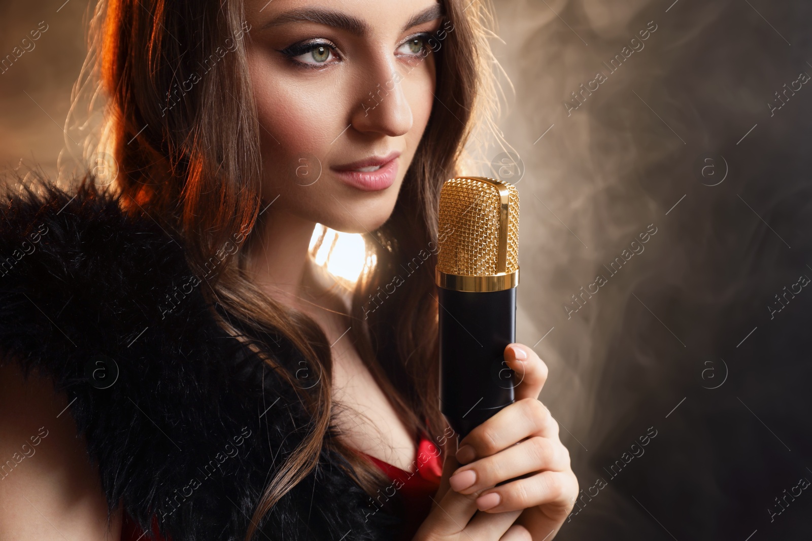 Photo of Beautiful young woman with microphone singing on color background with smoke, closeup. Space for text