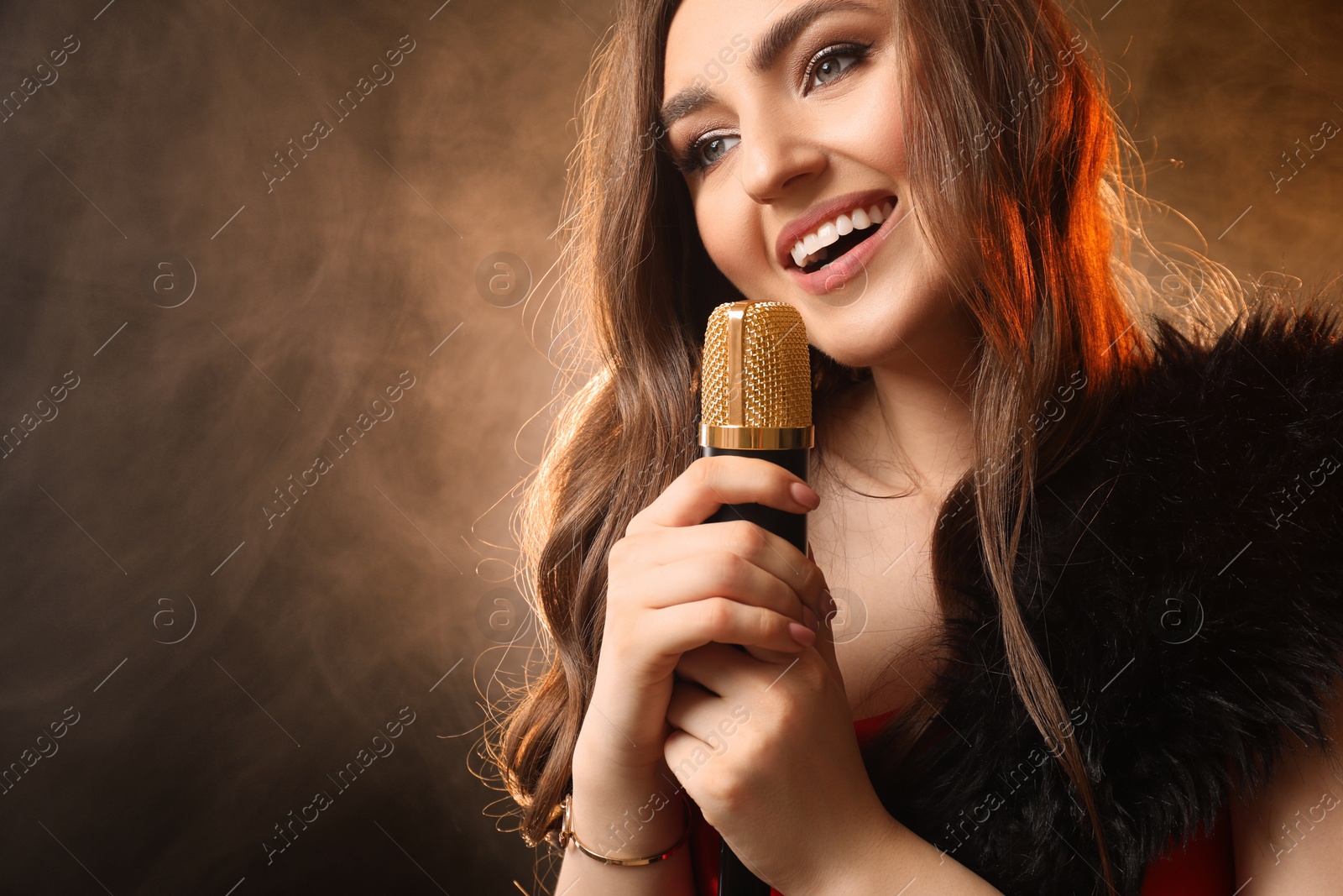 Photo of Beautiful young woman with microphone singing on color background with smoke, space for text