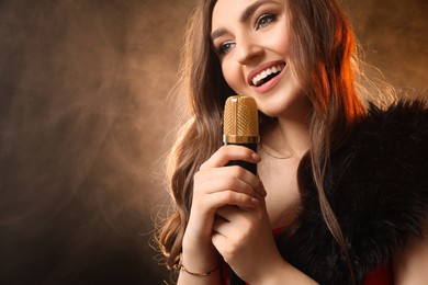 Photo of Beautiful young woman with microphone singing on color background with smoke, space for text