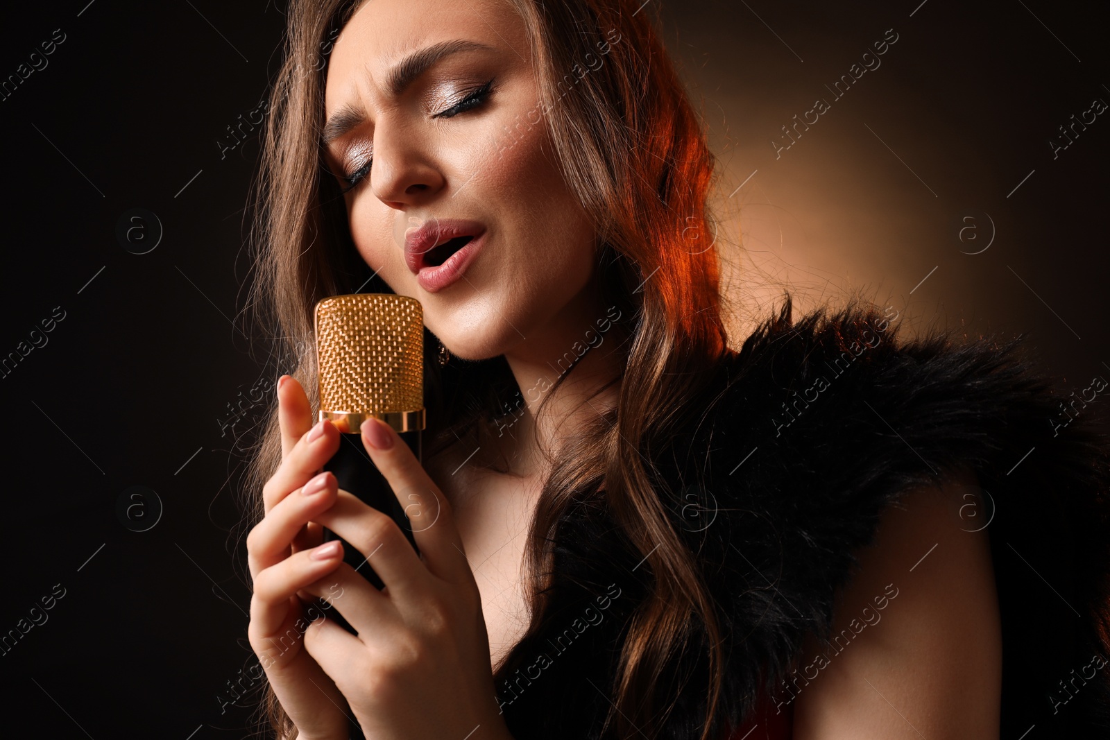 Photo of Beautiful young woman with microphone singing on dark background