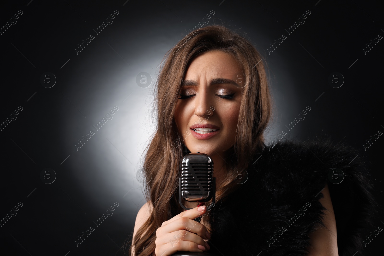Photo of Beautiful young woman with microphone singing on black background