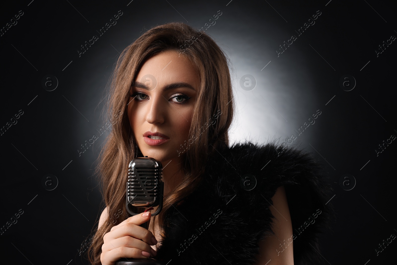 Photo of Beautiful young woman with microphone singing on black background